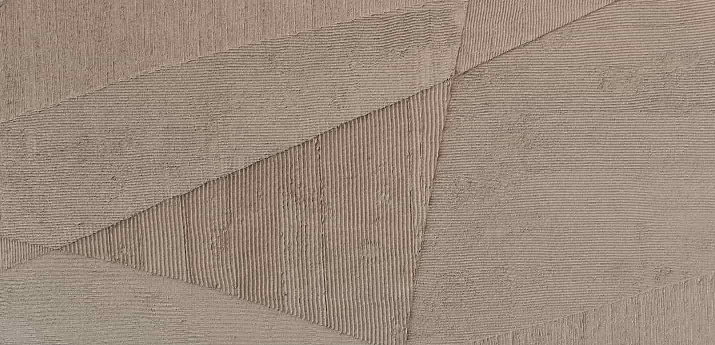 Detail of a textured wall surface with geometric patterns formed by hand-applied plaster in soft, earthy tones.