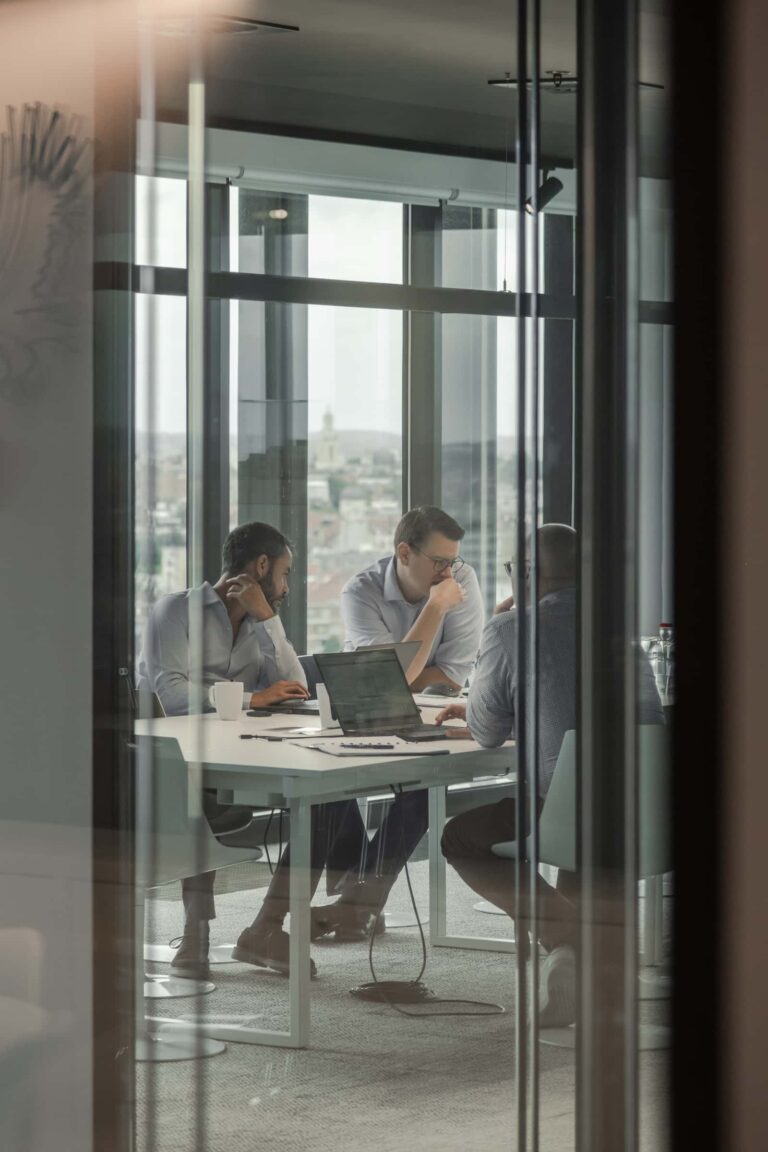 Team members in a glass-walled meeting room at Eaglestone, collaborating around a white table with laptops and notes, overlooking the city