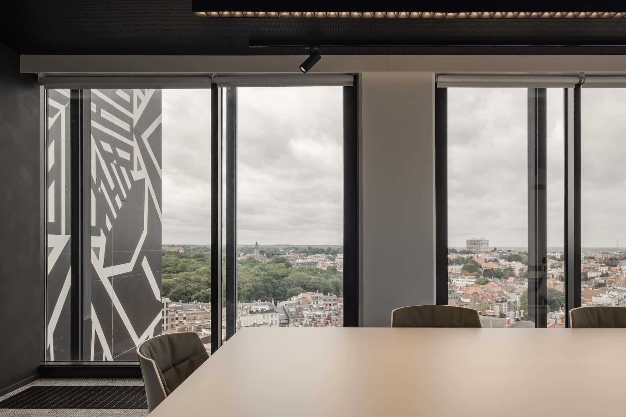 Conference room with a minimalist table and chairs, framed by floor-to-ceiling windows offering panoramic views of the city and adjacent building facade.