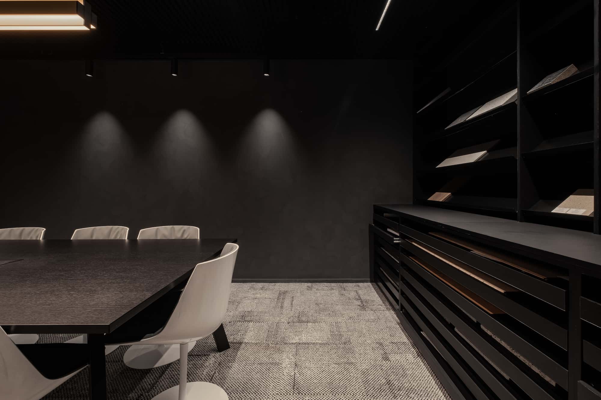 Interior view of a material library with dark shelving and a large meeting table, showcasing a variety of architectural finishes and textures.
