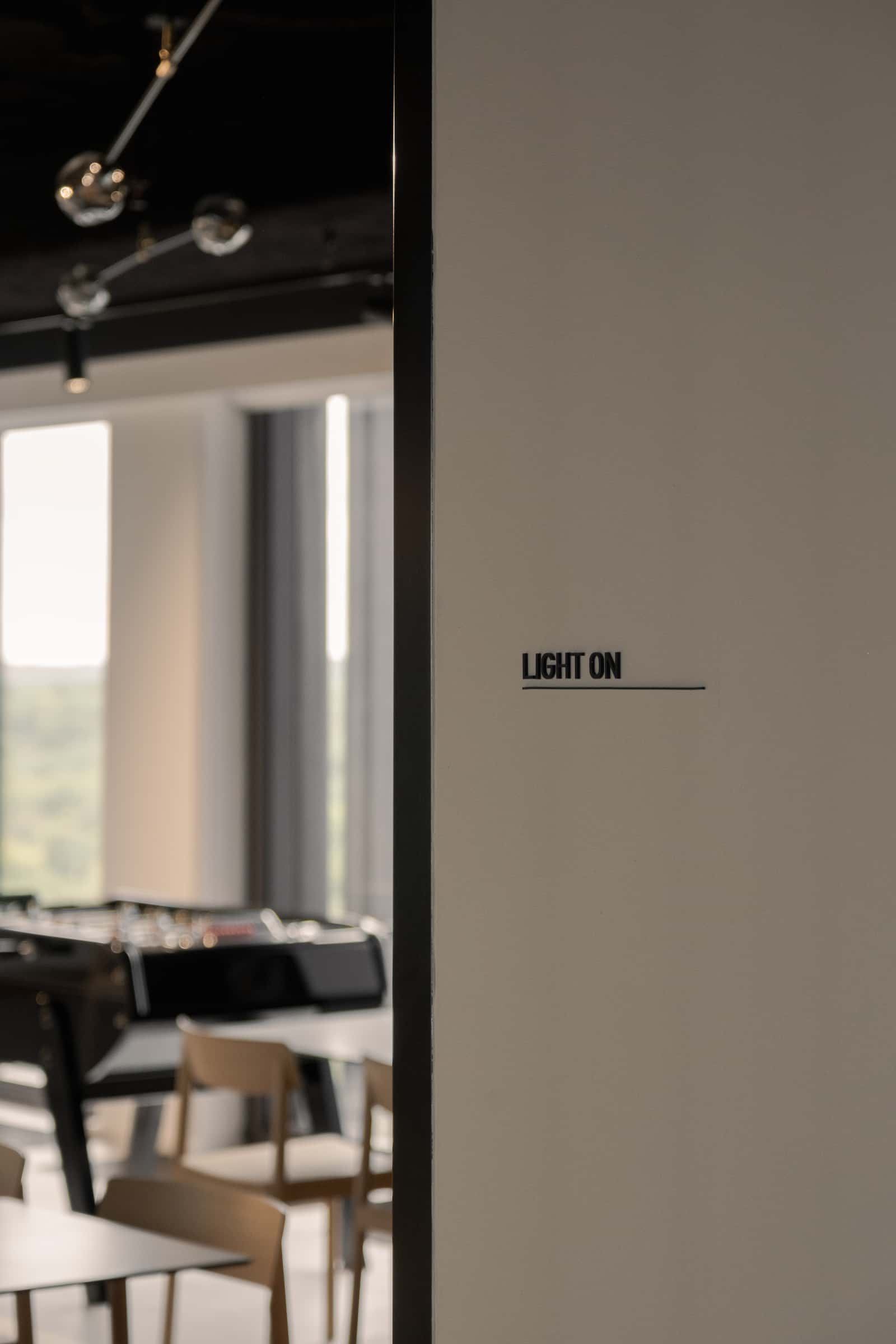 Wall detail with the words 'LIGHT ON' printed next to a bright and playful area featuring a foosball table and simple wooden chairs.
