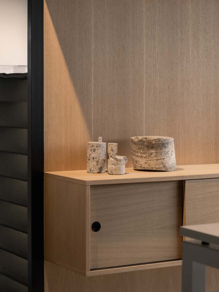 Close-up of sculptural concrete objects displayed on a light oak cabinet, against a wood-textured wall.