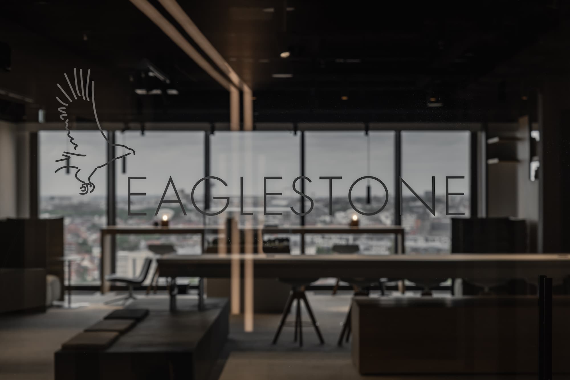 Eaglestone logo and eagle emblem seen on a glass partition, with a panoramic view of the workspace and city skyline in the background.