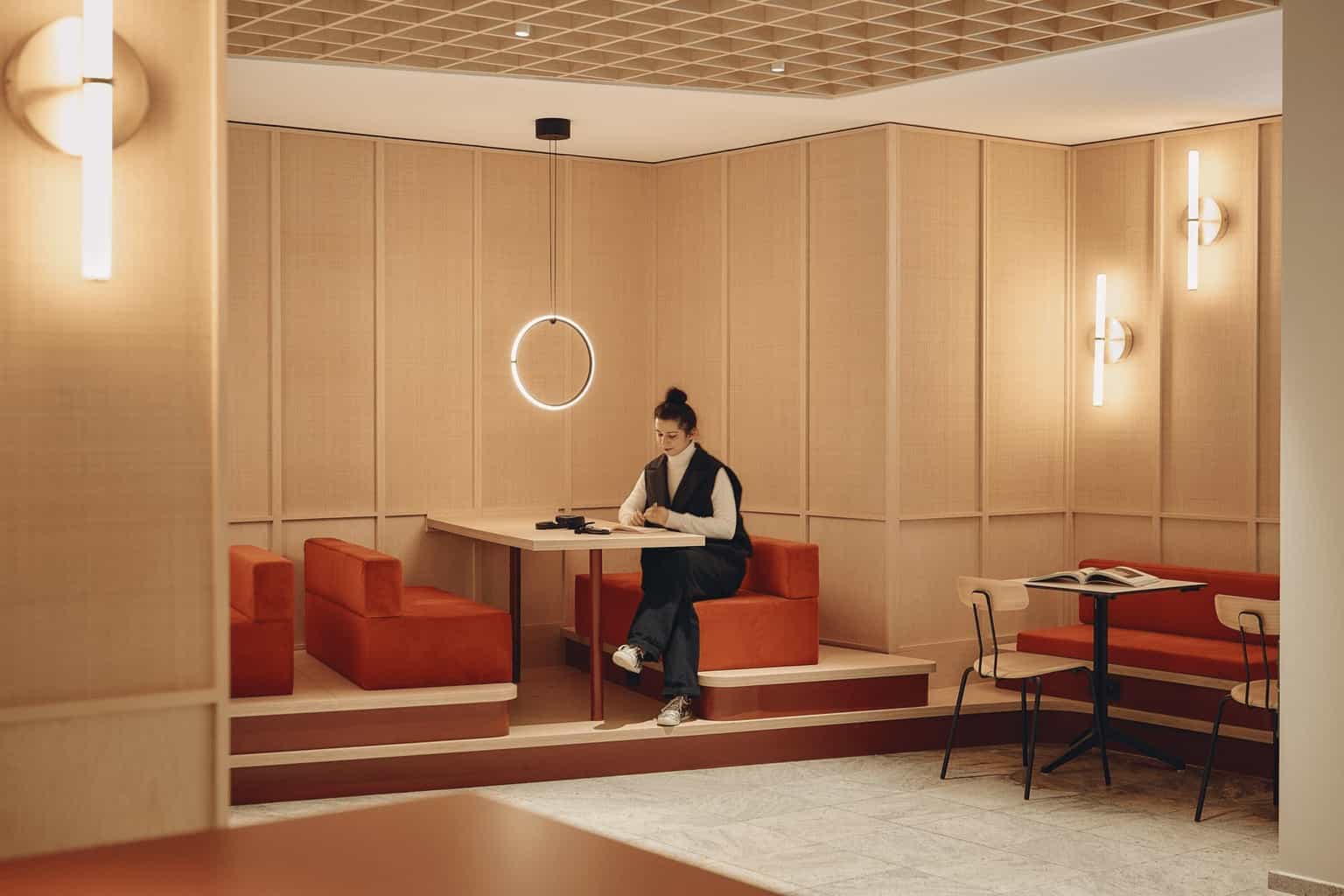 Person sitting and reading in a cozy built-in booth area illuminated by a ring light, surrounded by red cushions and beige wooden panels