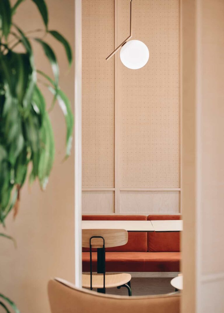 Framed view of a dining area with red upholstered bench seating, light wood panels, and a modern globe pendant lamp.