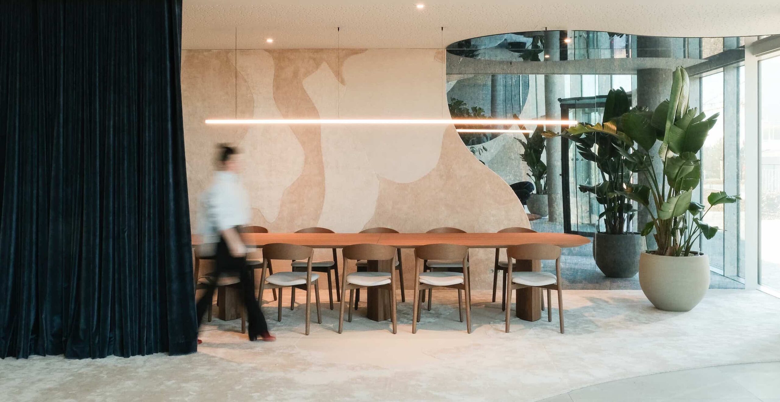 Contemporary dining area with long wooden table, natural-toned wall mural, and indoor plants, designed by ncbham for Xenon Building