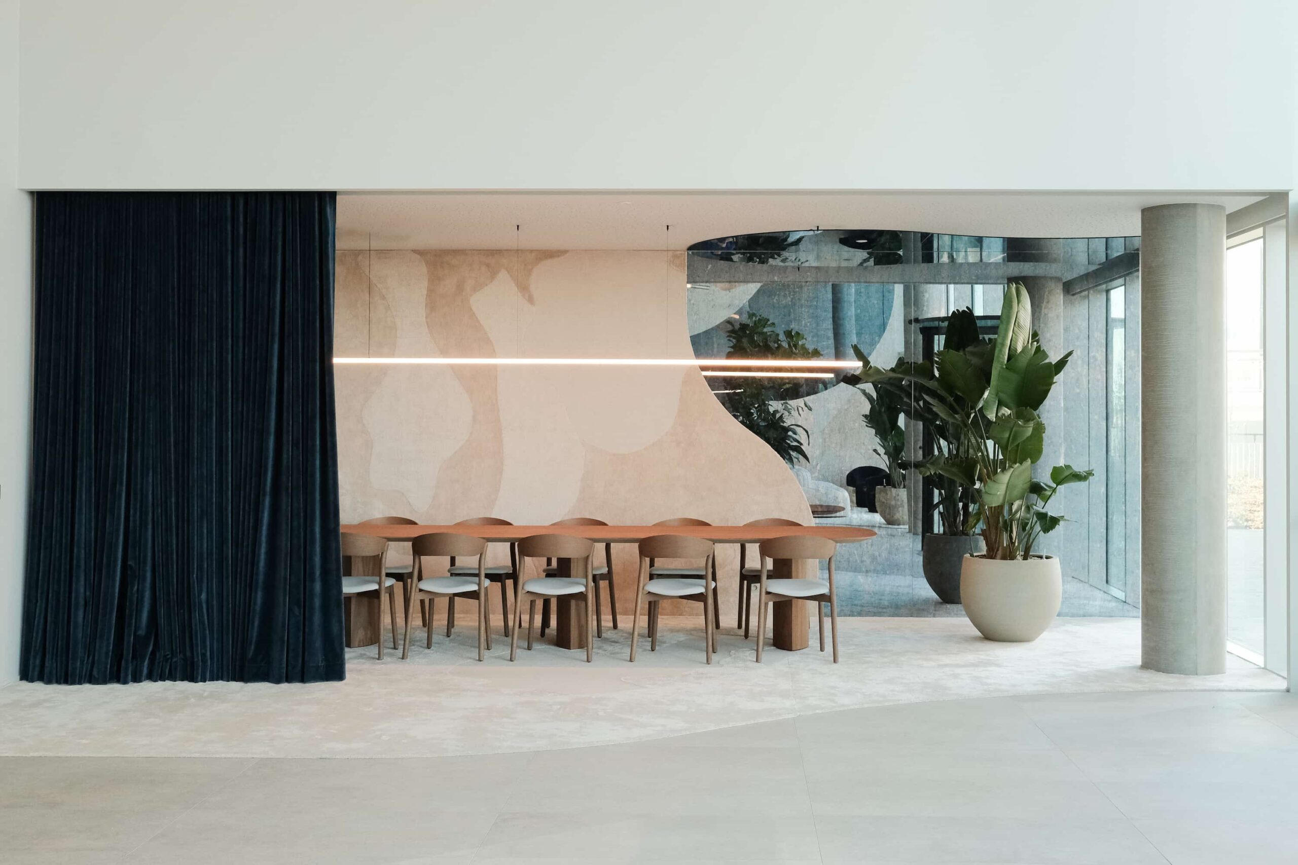 Full view of meeting area with wooden table, blue curtain, curved mirrored wall and large indoor plant