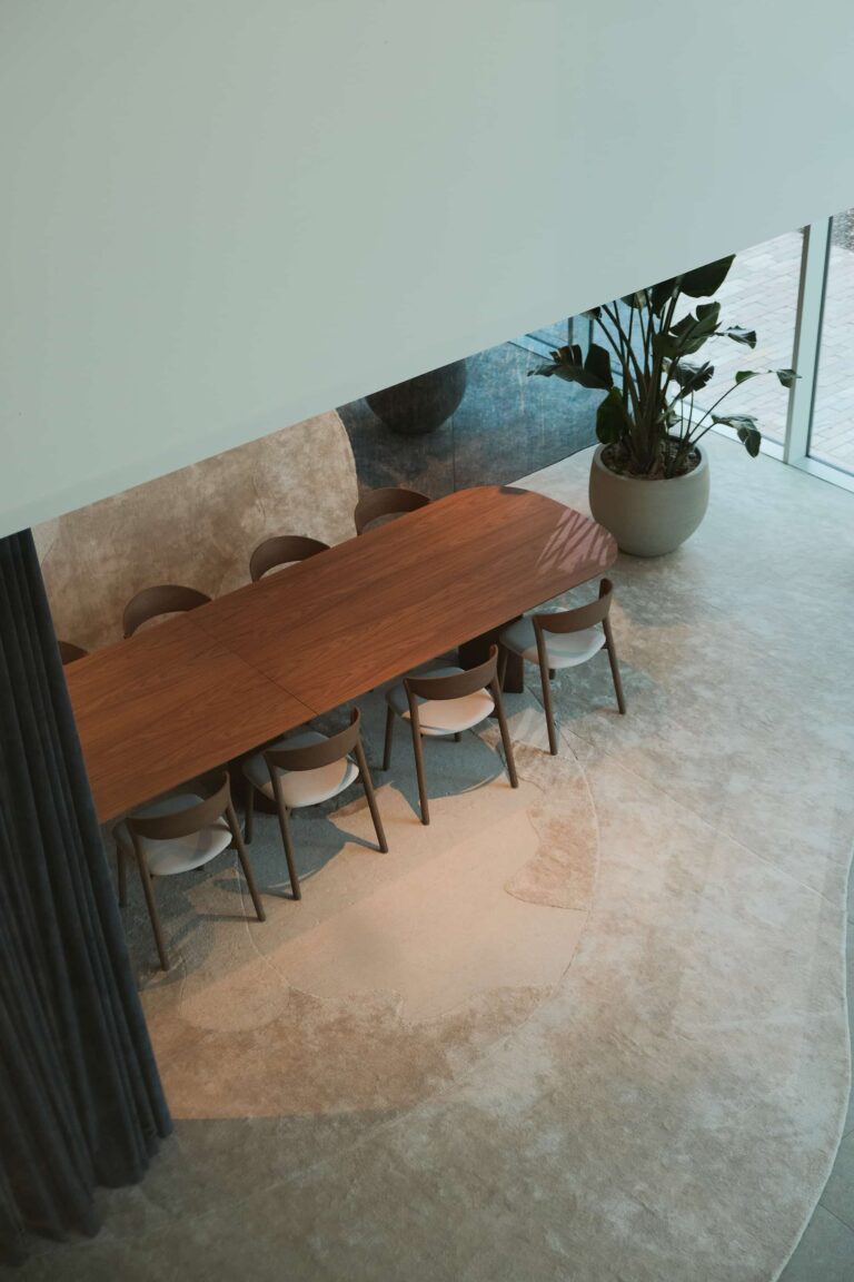 Overhead view of minimalist meeting space with sculptural rug, wooden table and chairs by the window