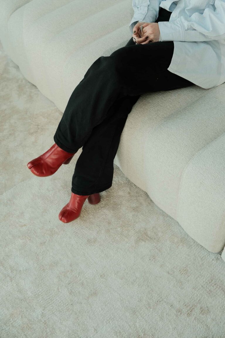Close-up of person wearing red leather boots sitting on a soft-textured white modular bench