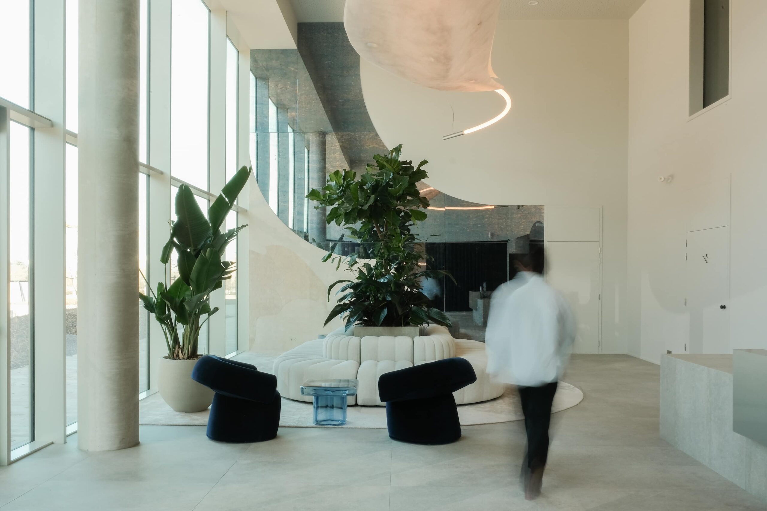 Elegant lounge with curved white sofa, velvet chairs, large indoor plants, and sculptural lighting in Xenon Building