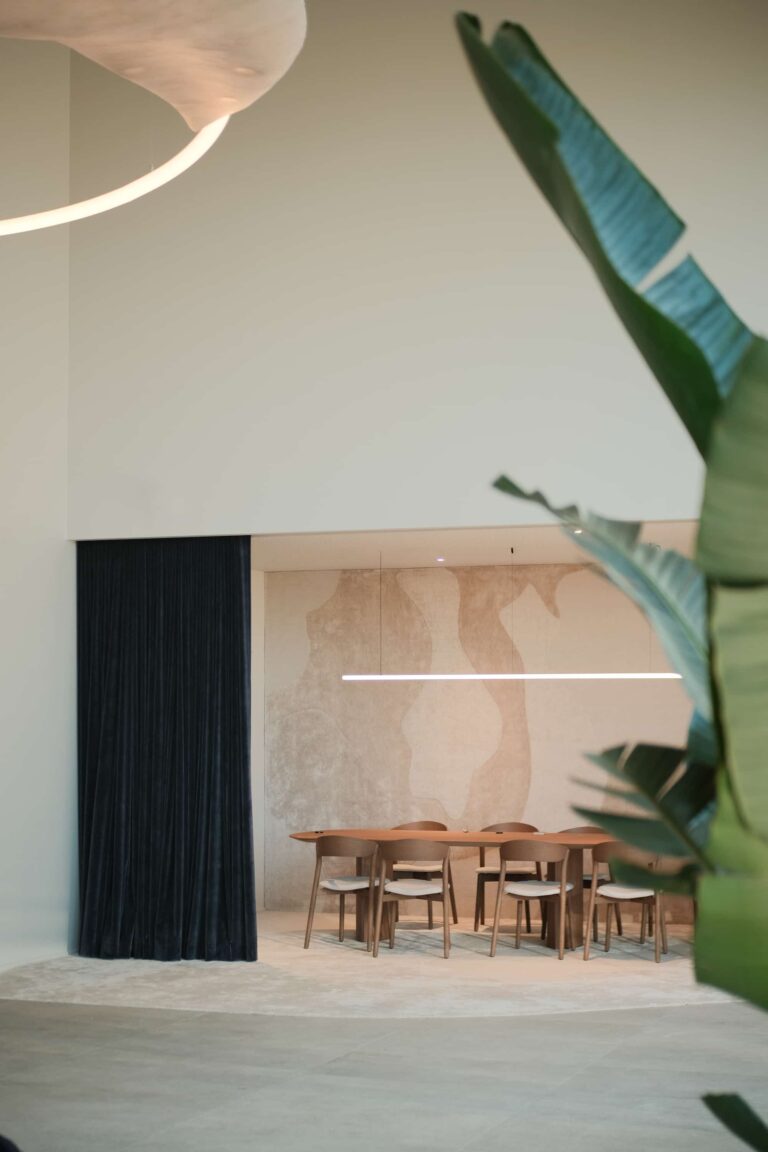 Large wooden meeting table with sculptural wall backdrop, surrounded by wooden chairs and soft velvet curtain