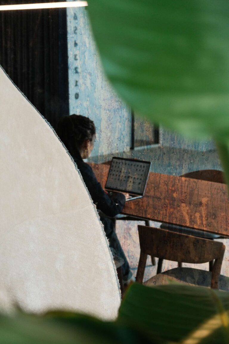 Person working on a laptop reflected in curved mirror, surrounded by soft textures and abstract wall design