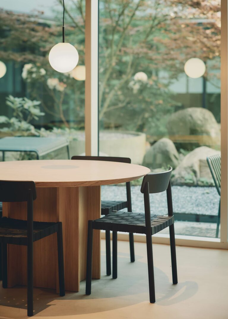 Minimalist furniture and honest materials frame a serene view of the garden. The large windows dissolve the boundary between inside and outside, turning the landscape into an integral part of the shared space.