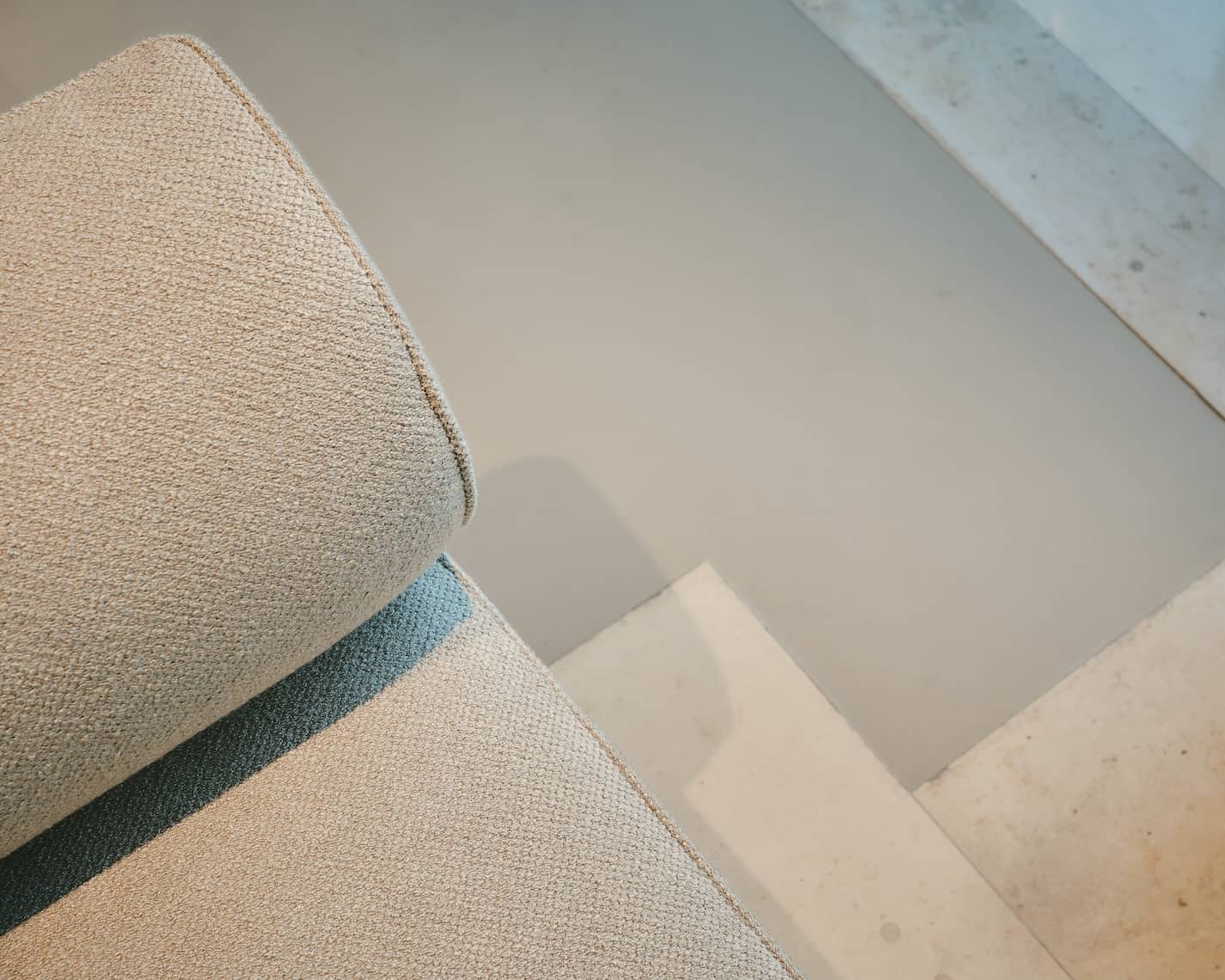 Close-up of a beige textured fabric sofa over a concrete and natural stone floor transition.