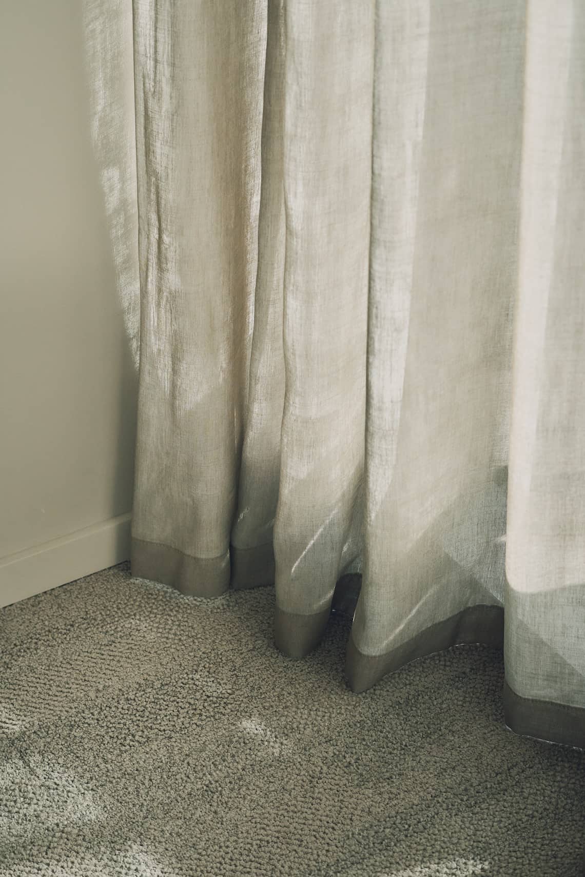 Light-filtering linen curtains draping softly over a textured carpeted floor.