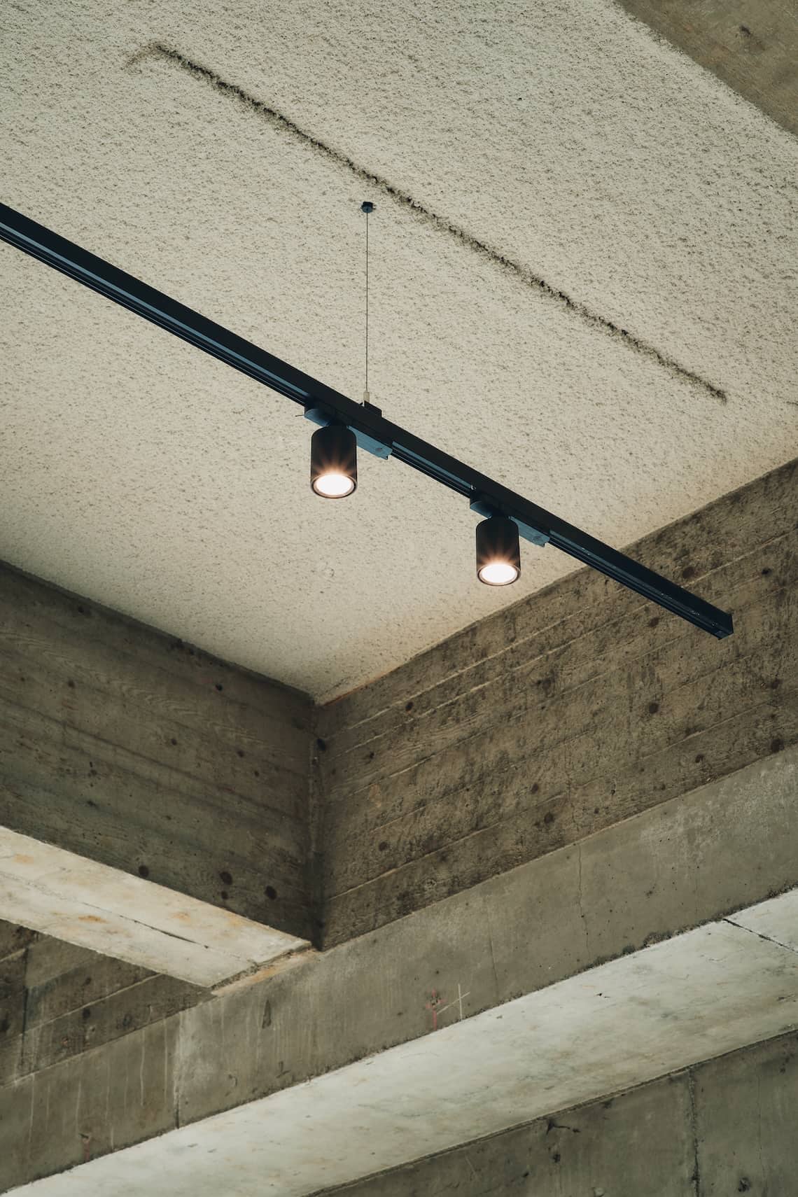 Minimal black ceiling spotlight track mounted on a textured white ceiling with exposed concrete beams.