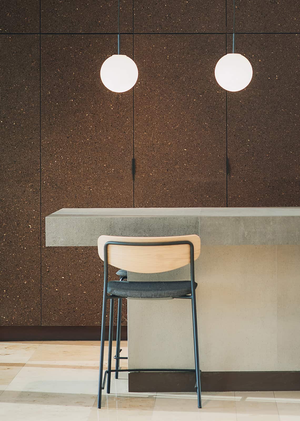 High chair at a concrete bar with dark cork paneling and spherical pendant lights.