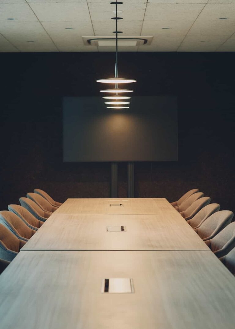 Long meeting table with integrated power outlets, surrounded by cushioned chairs and modern pendant lights.