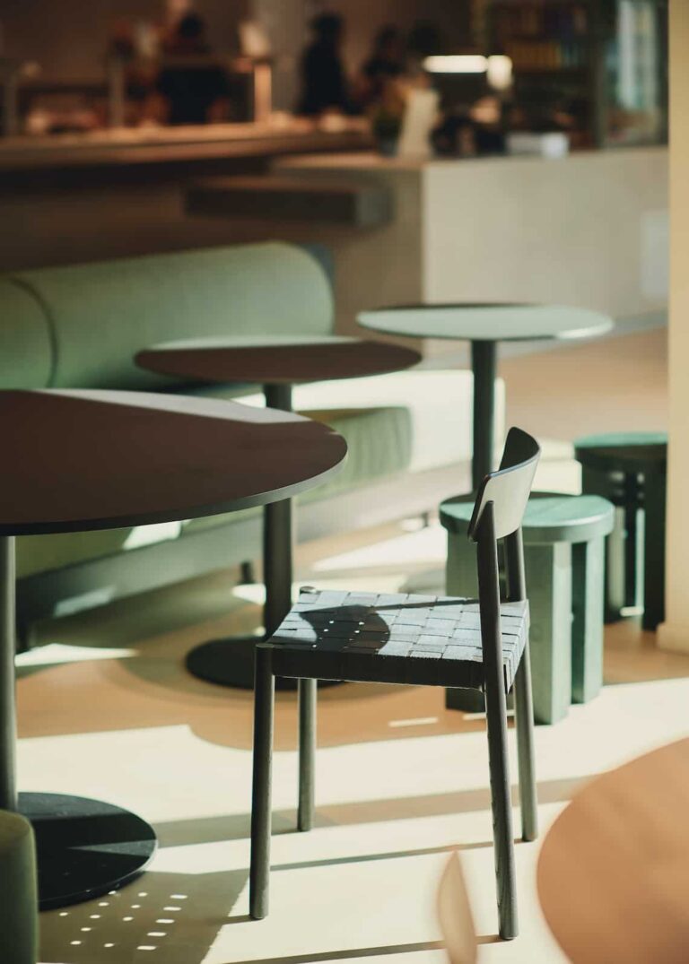 Modern green lounge chairs and round tables arranged in a well-lit interior with a soft, minimalist palette
