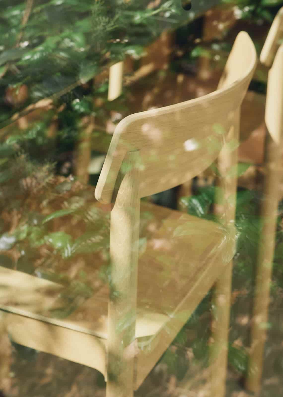 Wooden chair seen through a glass window with reflections of lush greenery from the outside garden.