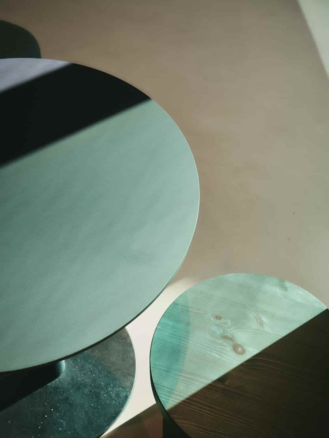 Top view of two green circular side tables illuminated by sharp sunlight, casting bold shadows.