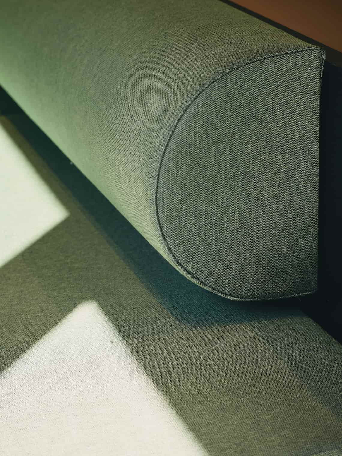 Close-up of a green bespoke bench with textured upholstery, partially in shadow.