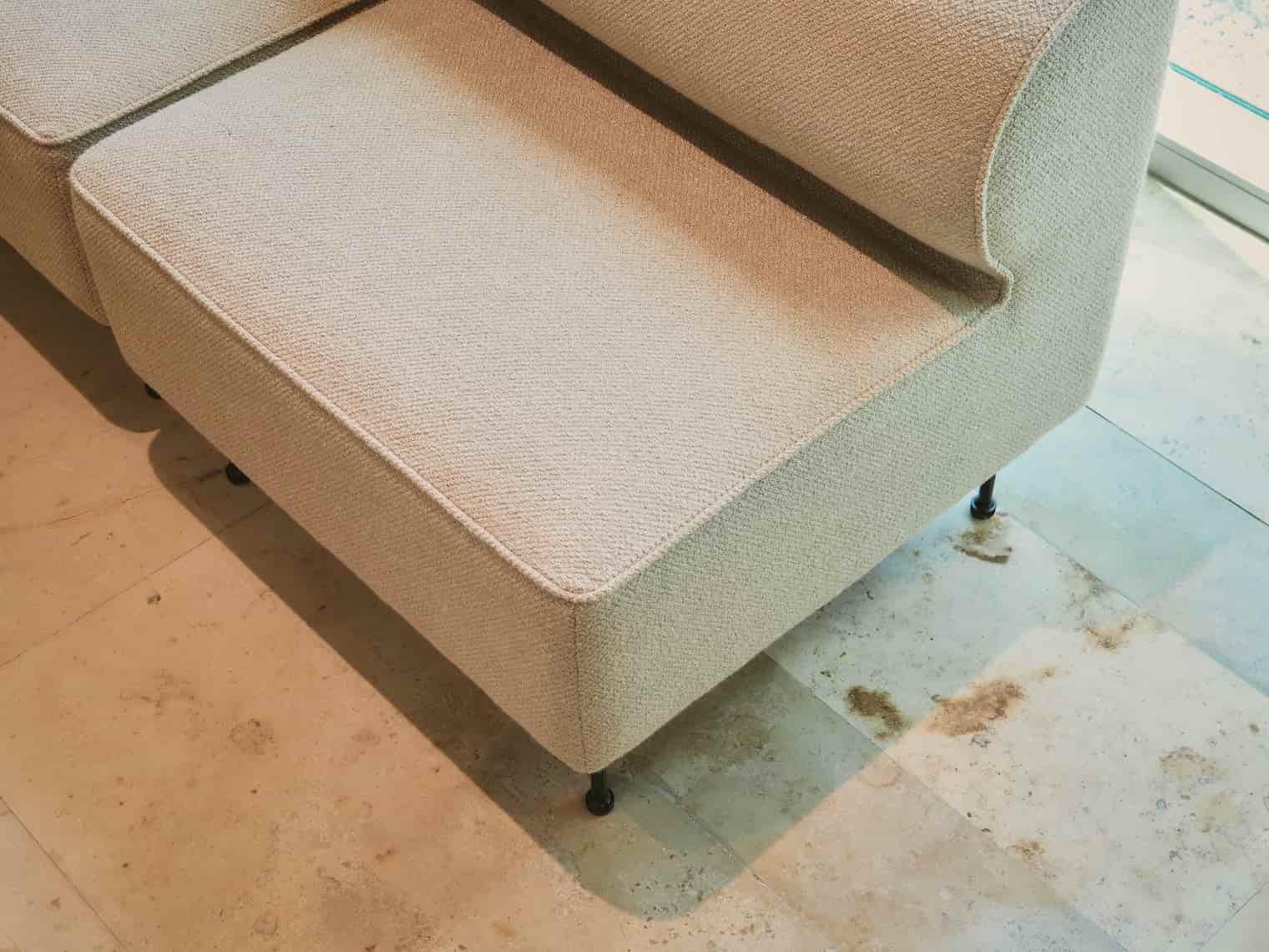 Close-up of a light beige upholstered modular sofa on a polished stone tile floor.